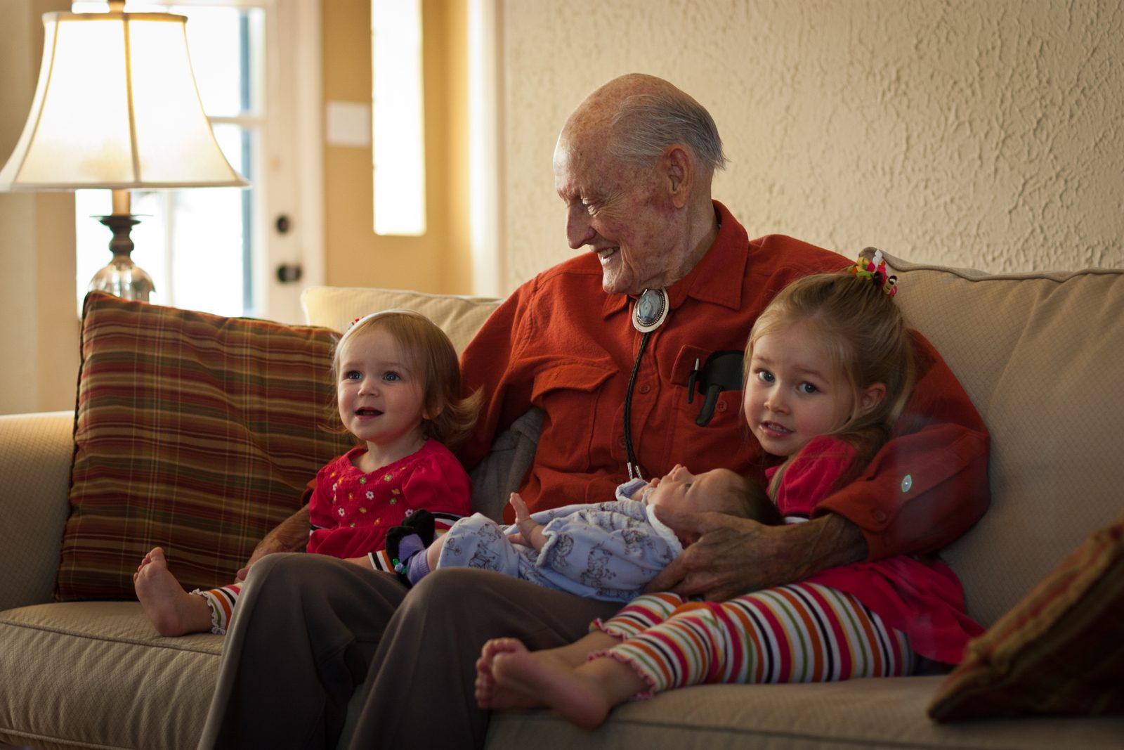 Duane smiling down at a newborn great-grandchild, two young girls beside him